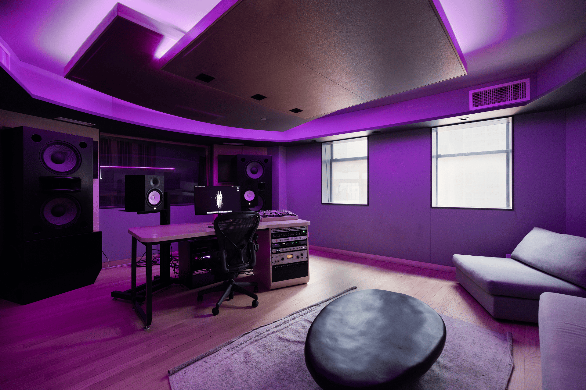 Wide view across Studio D with the desk, lounge seating, and purple ceiling lighting.