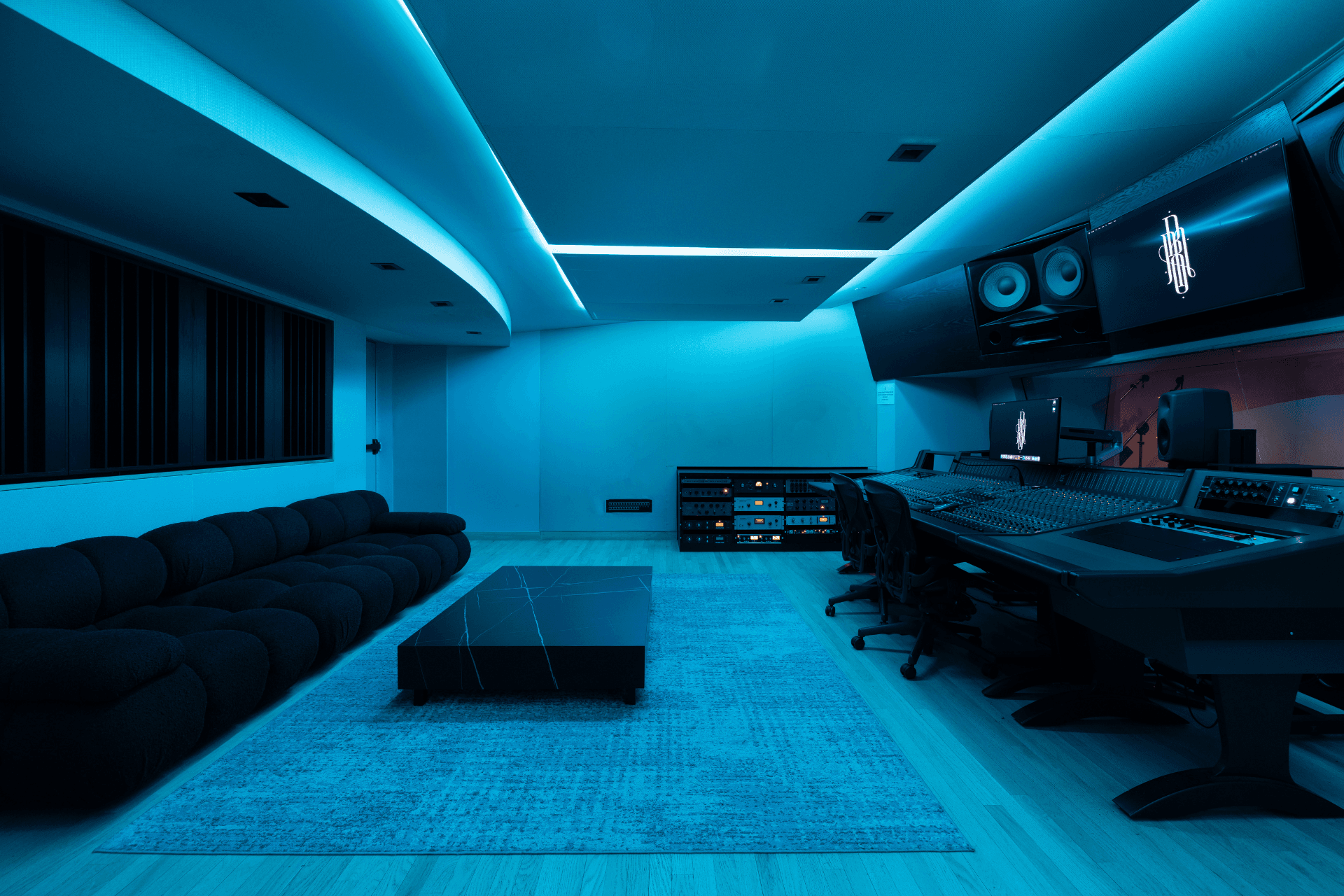 Wide control-room view of Studio B with the console, seating, and blue session lighting.