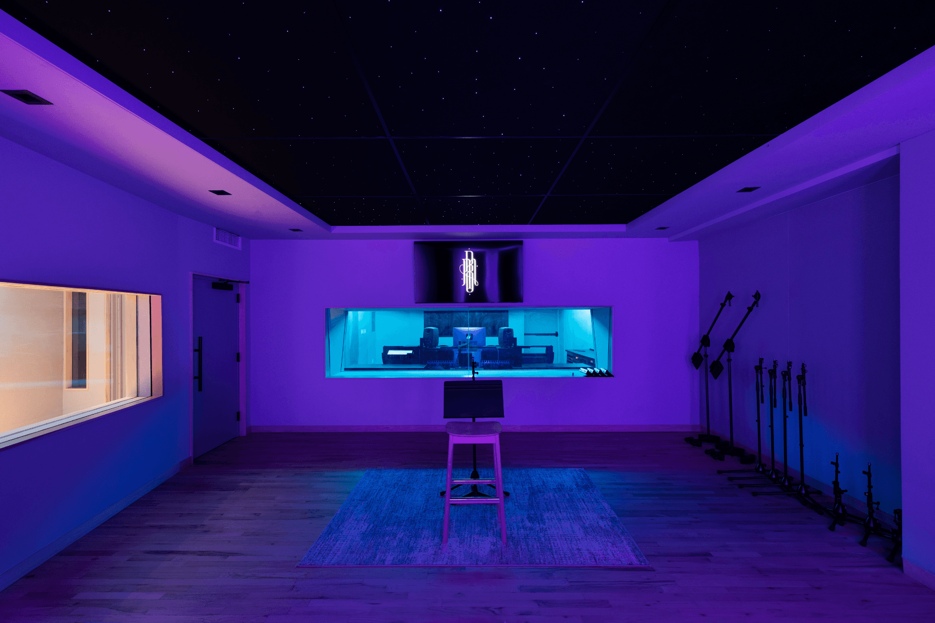 Purple-lit live room inside Studio B with piano, stool seating, and tracking space.