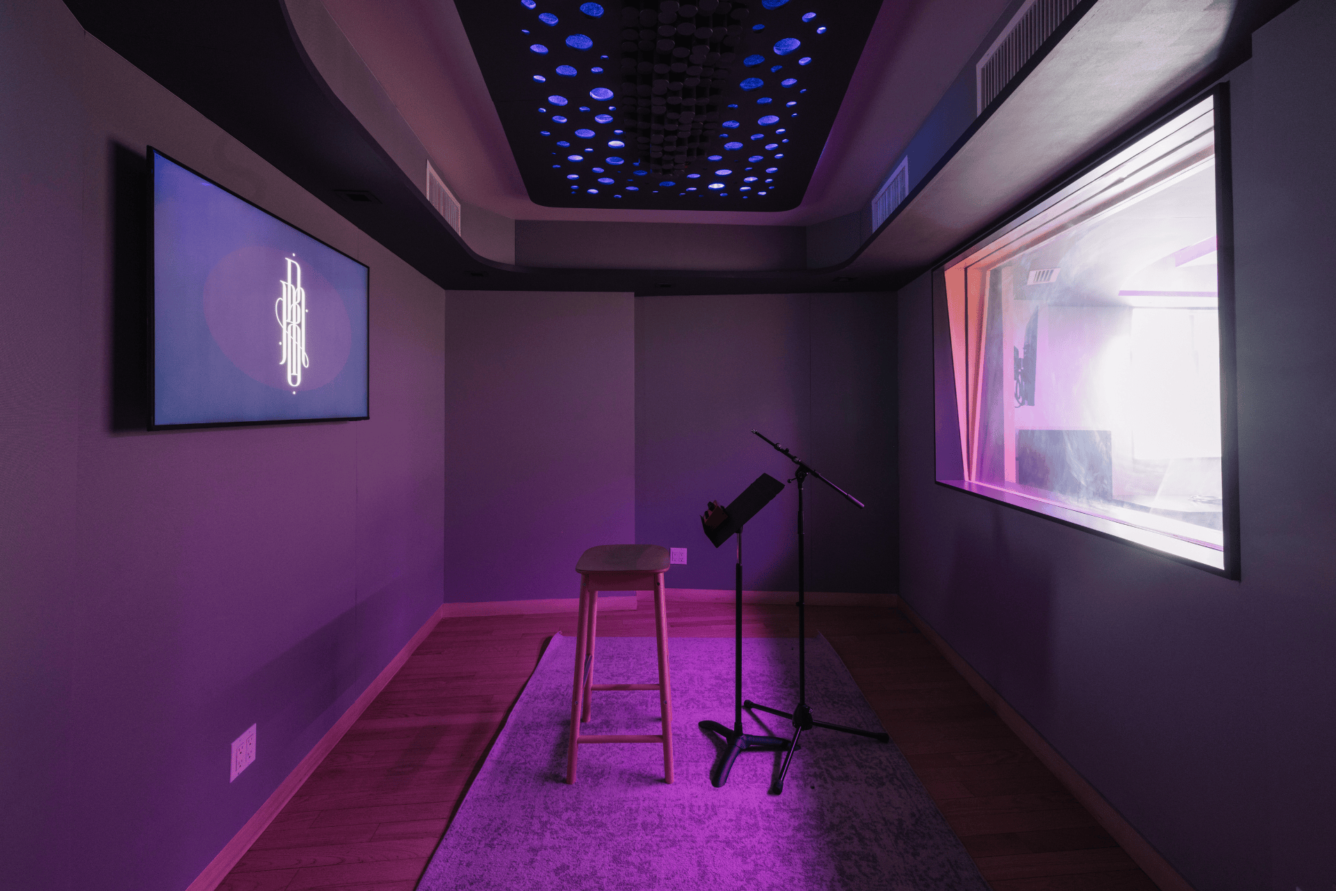 Studio D vocal booth with stool seating, mic stand, and window into the main room.