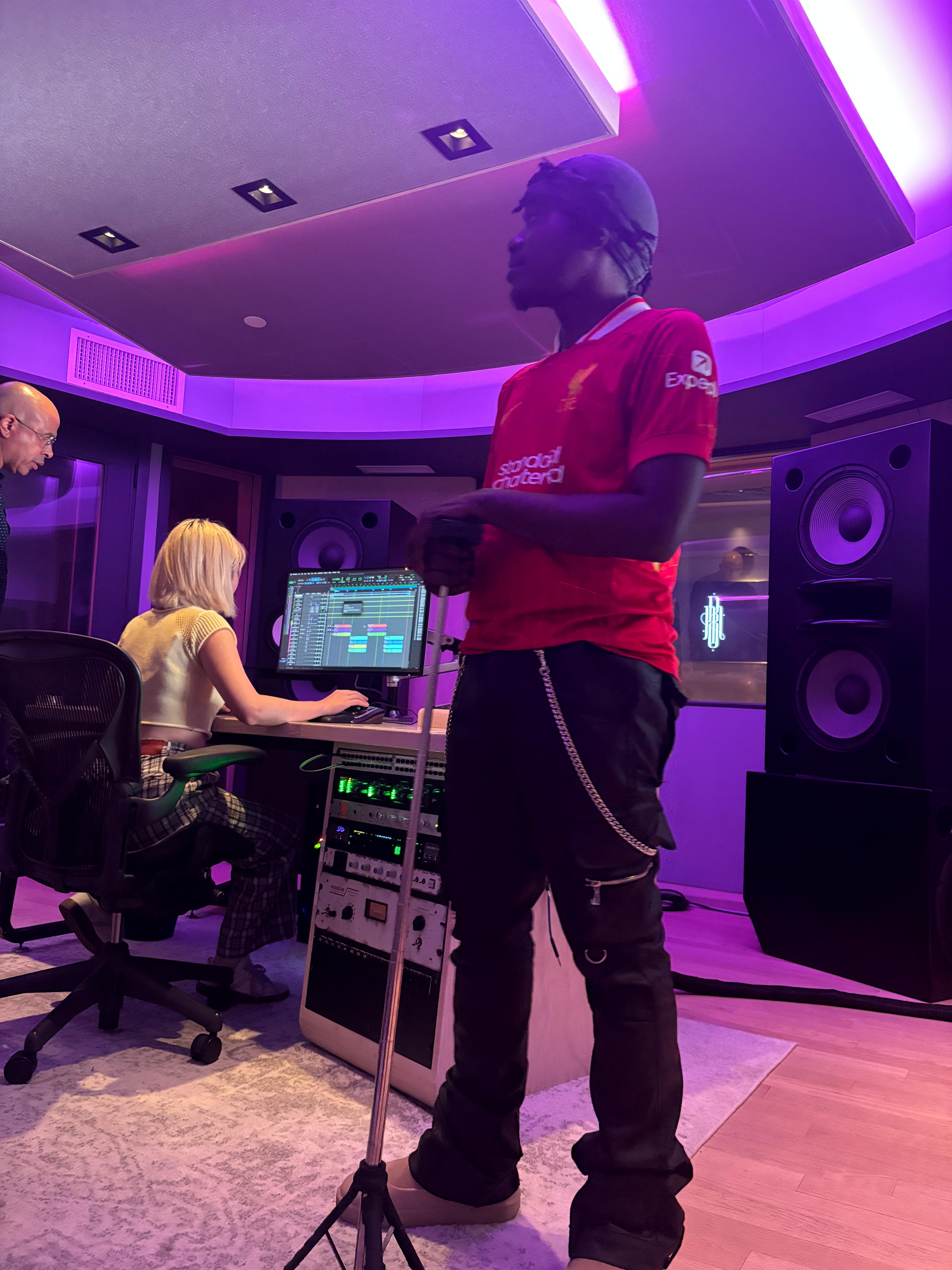 Session in Studio D with artists and engineer gathered at the desk under purple lighting.